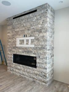 A modern fireplace with a whitewashed stacked stone surround and built-in shelving above the firebox.