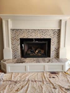 A fireplace with a herringbone tile surround and a marble hearth, framed by a white wooden mantel.