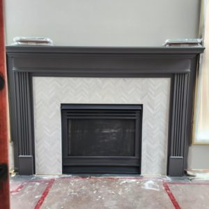 A fireplace with a herringbone tile surround and a dark gray wooden mantel.